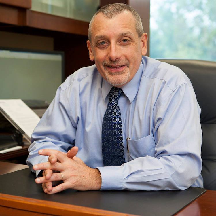 Man in shirt and tie sitting behind a desk.